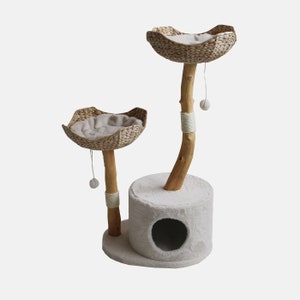 May include: A two-tier cat tree with a natural wood base and two woven baskets. The tree is beige in colour and features a round opening in the base for cats to enter.
