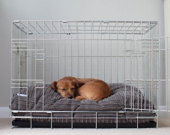 Könnte beinhalten: Ein brauner Hund schläft auf einem grauen Bett in einem silbernen Metallhundekäfig.