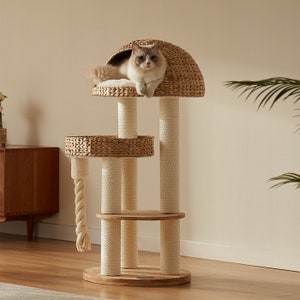 May include: A natural woven cat tree in beige and brown tones. The cat tree features a large, round, woven bed at the top, a smaller round bed in the middle, and a platform at the bottom. The cat tree has three sisal-covered scratching posts. A cat is sitting in the top bed.