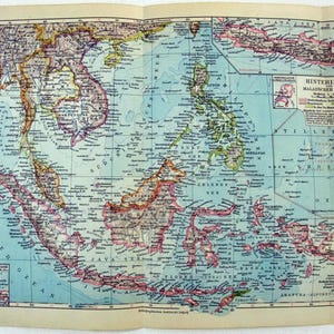 May include: A vintage map of Southeast Asia and surrounding islands, featuring countries like Thailand, Vietnam, and Indonesia. The map is colored with shades of blue, green, and brown, with detailed geographical features and place names. The map is printed on aged paper.
