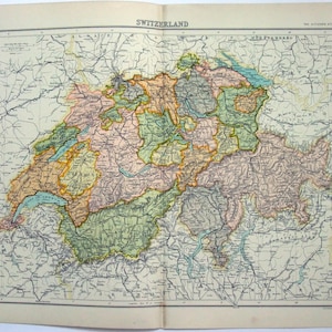 May include: A vintage map of Switzerland, featuring detailed geographical information. The map is colored with shades of green, orange, pink, and brown, highlighting different regions. The title "Switzerland" is printed at the top, with additional text and grid lines.