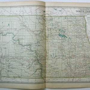 May include: A vintage map of North Dakota, showing county lines, towns, and railways. The map is printed on cream-coloured paper with a green and red colour scheme. The title "The Century Atlas North Dakota" is printed in the top right corner.