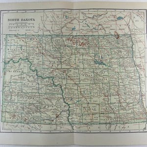 Może przedstawiać: Zabytkowa mapa stanu Dakota Północna, przedstawiająca szczegółowo hrabstwa, miasta i cechy geograficzne stanu. Mapa jest wydrukowana na postarzanym papierze, z tytułem "North Dakota" u góry. Mapa jest obramowana zieloną obwódką.