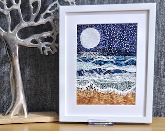 May include: A white framed artwork depicting a moonlit seascape with blue and white waves crashing on a sandy beach. The sky is filled with tiny white stars.