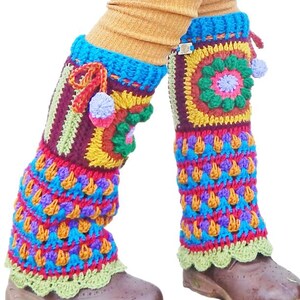 May include: Vibrant, handmade crochet leg warmers in a mix of colours. The design includes geometric patterns, pom-poms, and a scalloped edge. The leg warmers are worn over brown shoes and tan socks. The colours include blue, red, yellow, green, and purple.