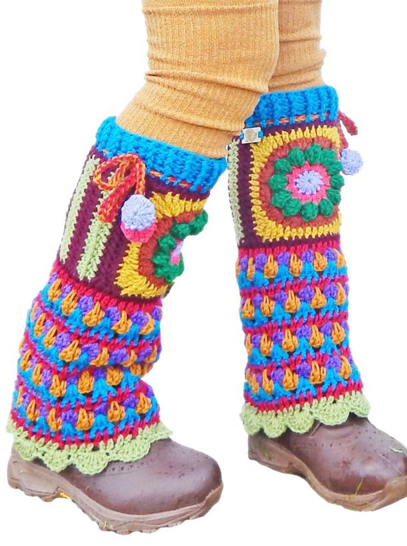 May include: Vibrant, handmade crochet leg warmers in a mix of colours. The design includes geometric patterns, pom-poms, and a scalloped edge. The leg warmers are worn over brown shoes and tan socks. The colours include blue, red, yellow, green, and purple.