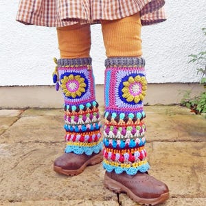 May include: Vibrant, handmade crochet leg warmers in a variety of colours, including pink, blue, yellow, and purple. The leg warmers, with a floral design, are worn over brown boots and mustard-coloured leggings. The crochet has a scalloped edge.