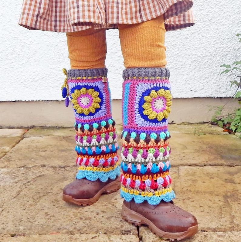 May include: Vibrant, handmade crochet leg warmers in a variety of colours, including pink, blue, yellow, and purple. The leg warmers, with a floral design, are worn over brown boots and mustard-coloured leggings. The crochet has a scalloped edge.