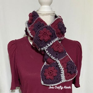 May include: A crocheted scarf with a repeating pattern of burgundy and grey flowers. The scarf is displayed on a white mannequin against a white background. The text "Jo's Crafty Hook" is visible at the bottom of the image.