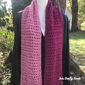 May include: A pink and magenta ombre crochet scarf with a delicate open stitch pattern. The scarf is draped over a mannequin wearing a black jacket. The text "Jo's Crafty Hook" is visible in the bottom right corner of the image.