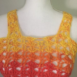 May include: A crocheted top with a yellow, orange, and red ombre design. The top has a square-shaped neckline and thin straps.
