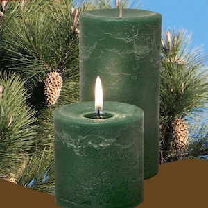 May include: Two green pillar candles, one lit, with a textured finish. The candles are in front of a pine tree branch.