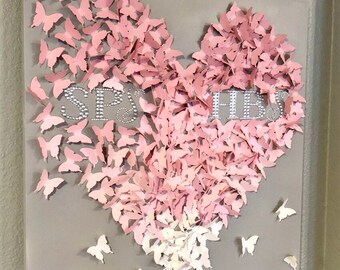 May include: A gray canvas with a heart shape made of pink and white paper butterflies. The word "SP" and "HER" are spelled out with rhinestones in the center of the heart.