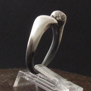 Puede incluir: Un anillo de plata con una banda redonda y lisa y una parte superior redondeada ligeramente elevada.