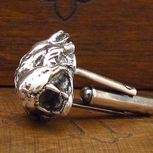 May include: Silver cufflinks featuring a detailed, three-dimensional sculpture of a snarling animal head.