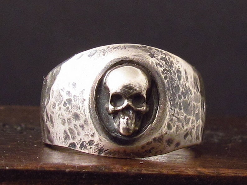 Pu&ograve; includere: Un anello d'argento con una fascia testurizzata e un design a forma di teschio al centro.