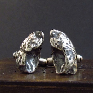 May include: A pair of silver cufflinks featuring a detailed, textured design of two frogs facing each other.