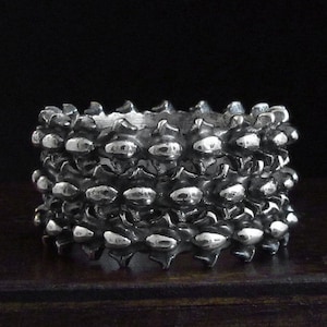 May include: A silver ring with a textured design that resembles a stack of overlapping scales.