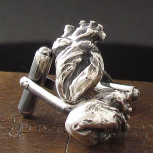 May include: Silver cufflinks in the shape of a human heart. The cufflinks are detailed and realistic.