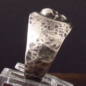 Pu&ograve; includere: Un anello d'argento con una fascia testurizzata e un design a forma di teschio. Il teschio &egrave; dettagliato e ha una finitura martellata ruvida.