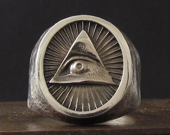 Peut inclure: Une bague en argent avec une bande texturée et un motif circulaire représentant un œil qui voit tout à l'intérieur d'un triangle.
