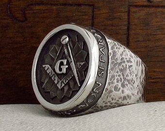 May include: A silver Masonic ring with a textured band and a circular top featuring a compass and square with a letter "G" in the center. The band is inscribed with the words "Non Separari".