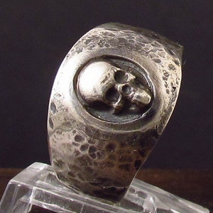 Pu&ograve; includere: Un anello d'argento con un design a forma di teschio. L'anello &egrave; testurizzato e ha una finitura martellata.