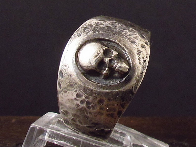 Pu&ograve; includere: Un anello d'argento con un design a forma di teschio. L'anello &egrave; testurizzato e ha una finitura martellata.