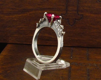 May include: A silver ring with a large red gemstone and intricate floral details on the band.