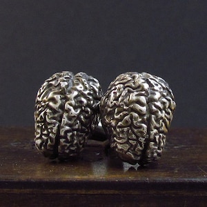 May include: Two silver brain-shaped cufflinks. The cufflinks are detailed with a textured surface that resembles the folds of a human brain.