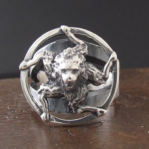 Könnte beinhalten: Ein silberner Ring mit einem dreidimensionalen Design eines Löwenkopfes mit drei Beinen.