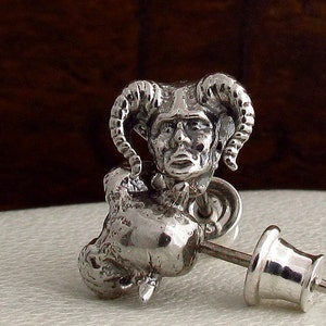 Può includere: Orecchino d'argento con una scultura dettagliata di una figura cornuta con un viso umano. La figura indossa una corona e ha una piccola scultura animale dettagliata ai suoi piedi.