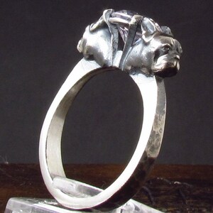 Può includere: Un anello d'argento con due teste di cane scolpite sulla parte superiore. L'anello è testurizzato e ha una finitura martellata.