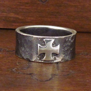 Könnte beinhalten: Ein silberner Ring mit gehämmerter Oberfläche und einem erhabenen Kreuzdesign.