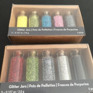 May include: Two boxes of glitter jars, each containing five small glass bottles filled with colorful glitter. The glitter colors include yellow, green, blue, pink, silver, red, lime green, and dark gray. The text on the box reads "Glitter Jars" and "5 - 0.127 oz / 3.6 g."