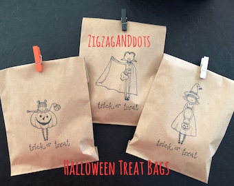 May include: Three brown paper Halloween treat bags with black and white illustrations of a pumpkin-headed girl, a vampire, and a witch. Each bag has the words "trick or treat" and is clipped with a clothespin. The text "ZIGZAGANDDOTS" and "HALLOWEEN TREAT BAGS" are also visible.