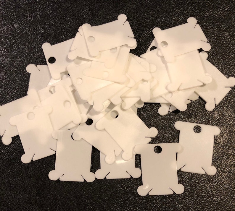 May include: A pile of white plastic thread bobbins. The bobbins are used to hold thread for sewing or embroidery.