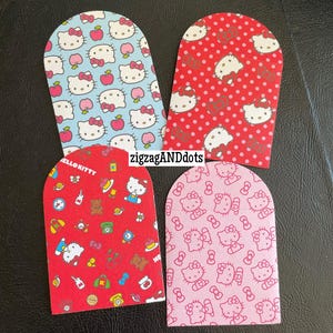 May include: Four mini envelopes with rounded tops, each featuring a different pattern. The patterns include Hello Kitty characters, apples, and other designs on a light blue, red, and pink background. The text "MINI ENVELOPES" is at the top.