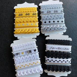 May include: Four sets of ribbon trim on white card stock. Each set includes five different trims, including a black and white polka dot trim, a black and white wavy trim, a black trim with the text "Life is an Adventure", a black and white trim with a bicycle design, and a black and white trim with the text "Happy Fun".