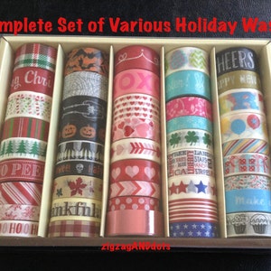 May include: A complete set of holiday themed washi tape rolls in a clear plastic box. The rolls are arranged in rows and include designs such as Christmas trees, candy canes, pumpkins, hearts, stars, and cupcakes.