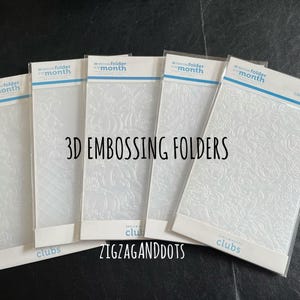 May include: Five white plastic embossing folders with a 3D design. The folders are labeled "folder of the month" and have the names "Zigzaganddots", "Clubs" and "Clubs" printed on them.
