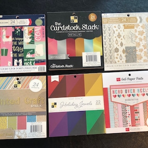 May include: A collection of six paper crafting supplies, including cardstock, patterned paper, and paper pads. The cardstock is metallic and comes in a variety of colors. The patterned paper features a winter theme with snowflakes and ornaments. The paper pads are 6x6 inches and feature a variety of patterns and colors.