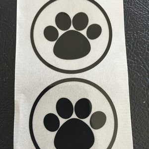 May include: A sheet of white sticker paper with three black paw print stickers. Each sticker has a black paw print inside a black circle.
