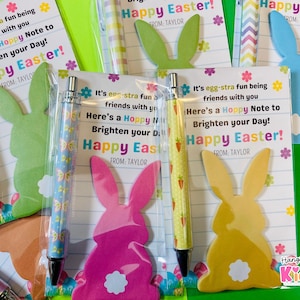 May include: An assortment of Easter-themed gifts, including pens and bunny-shaped notecards. The pens have colorful designs, and the cards feature the text "Happy Easter!" and "Here's a Hoppy Note to Brighten your Day!" with a bunny silhouette.