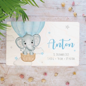 Könnte beinhalten: Eine Holzplakette mit einer blauen und weißen Aquarell-Illustration eines Elefanten in einem Heißluftballon. Die Plakette trägt den Namen "Anton" und enthält das Datum "31. Dezember 2021", das Gewicht "3.410 g", die Länge "54 cm" und die Uhrzeit "09:46 Uhr".