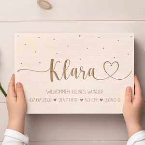 May include: A wooden sign with the name Klara engraved in cursive script, surrounded by small stars. The sign also includes the text "Willkommen kleines Wunder" and the date 07 07 2021, time 21:47 Uhr, weight 3.640 g, and length 53 cm.