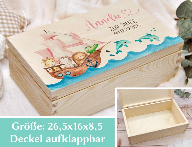 May include: A wooden box with a hinged lid, decorated with a watercolor illustration of a pink sailboat with animals on board, sailing on blue water with dolphins. The box is 26.5 inches by 16 inches by 8.5 inches and has the name "Annelie" and the text "Zur Taufe am 12.02.2022" on the lid.