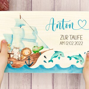 May include: A wooden sign with a blue and white sailboat with animals on it. The sign says "Anton zur Taufe am 12.02.2022" and has a blue heart.