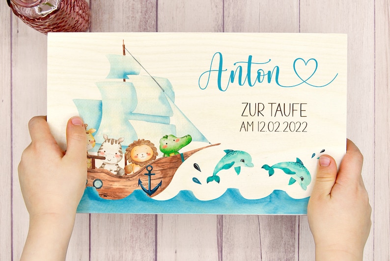 May include: A wooden sign with a blue and white sailboat with animals on it. The sign says "Anton zur Taufe am 12.02.2022" and has a blue heart.