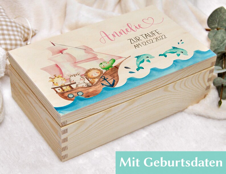 May include: A wooden keepsake box with a pink and blue nautical theme. The lid features a ship with animals, a heart, and the text "Annelie zur Taufe am 12.02.2022".